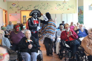 Energetic dancers perform for a roomful of elderly residents in wheelchairs during a festive event.